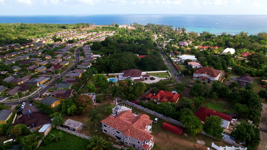 Aerial orbit of dense home neighborhoods in middle of Jamaica lush tropical hills and coastline showcasing natural beauty