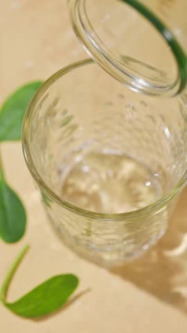 freshly made green spinach and banana smoothie flows into a glass from a bottle on a sunny light table surface