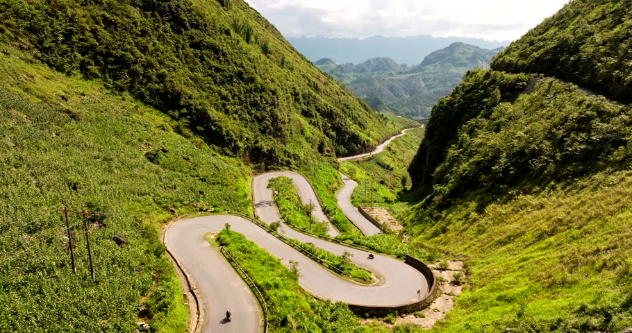 Motorcycles drive down curvy Ha Giang Loop of Tham Ma Pass Vietnam, aerial