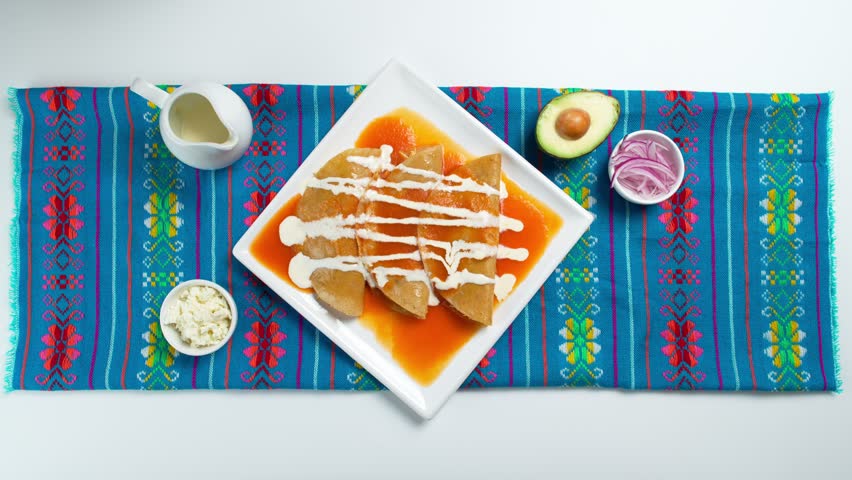 Typical mexican dish, red enchiladas, latina woman spreads crumbled cheese over a plate with red enchiladas