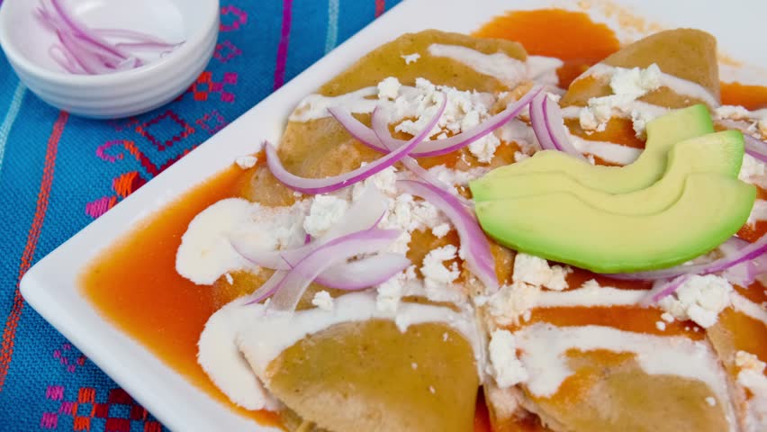 Authentic Mexican food, red enchiladas with cream, cheese, julienned onions and avocado