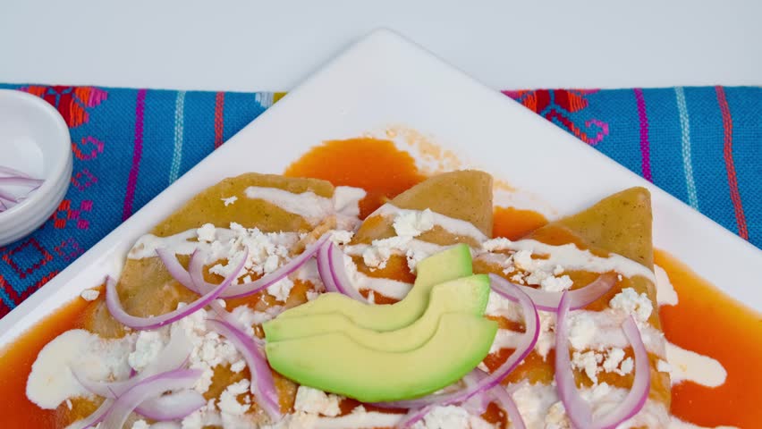 Mexican food, red enchiladas with cream, cheese, julienned onions and avocado on top