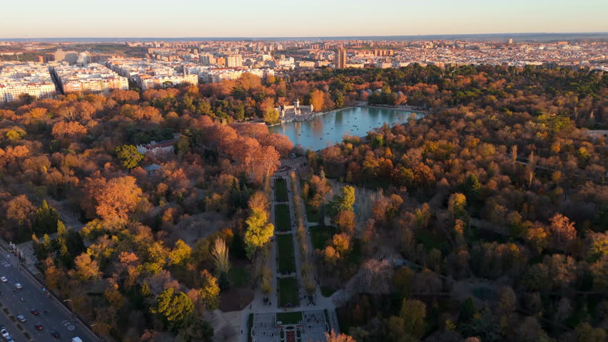 Stunning aerial drone view captures the beauty of El Retiro Park in Madrid, showcasing its vibrant colors and tranquil lake, providing a contrast to the bustling urban landscape of the city