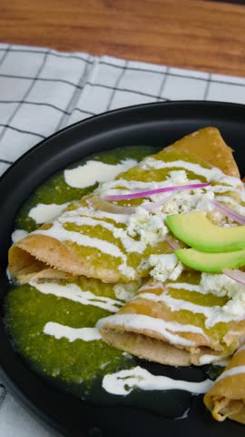 Vertical video, Mexican food, green enchiladas with chicken, mexican cream, crumble cheese, avocado and red onion