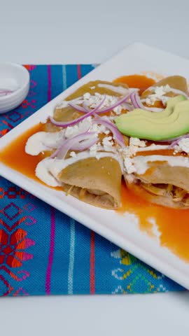 Vertical video, Authentic Mexican food, red enchiladas with cream, cheese, julienned onions and avocado