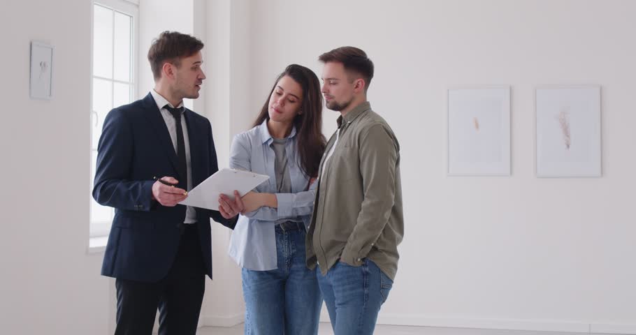 Young couple searching new apartments for life agent realtor showing another real estate object new apartments for young couple. Expertise of realtor who navigates couple through new apartments