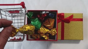 A man's hand moves colorful, expensive foil-wrapped candies from a box to a toy shopping cart. Buying gift candies.  - Powered by Shutterstock - Get 15% off with code: PIKWIZARD15