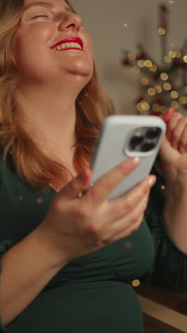 Shocked amazed Caucasian woman girl lady received great news on smartphone while sitting on sofa at home during winter New Year Christmas Xmas holidays. Girl reads a pleasant message on the phone