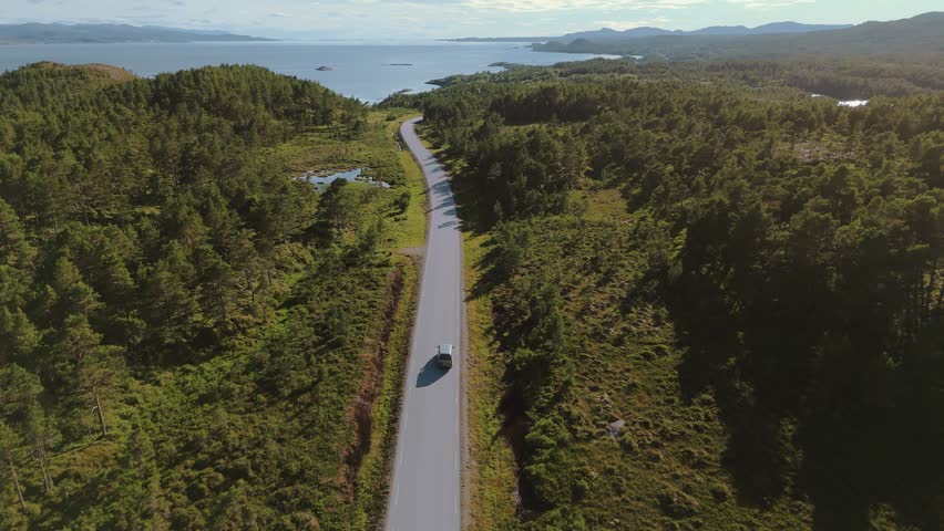 Modern camping van car driving towards the sea on a country road in Norway. Traveling road trip aerial Scandinavia.
