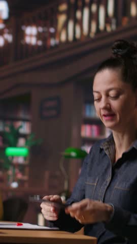 Vertical Video Noisy person disturbing people at the library by speaking very loud, being rude and answering a phone call in the study area. Disruptive annoying woman asked to keep silence. Camera B.