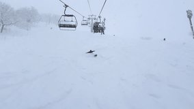 POV: Snowy ride up a ski lift in Niseko, Japan. Snowboarders and skiers carve the powdery slopes below, while fellow riders on the lift sit bundled in winter gear, enjoying Hokkaido’s alpine views - Powered by Shutterstock - Get 15% off with code: PIKWIZARD15