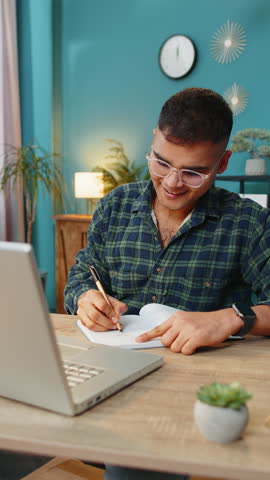 Indian man student freelancer study with notebook write notes making conference video call talking to webcam on laptop computer. Online teacher e-learning in remote chat. Distance education online