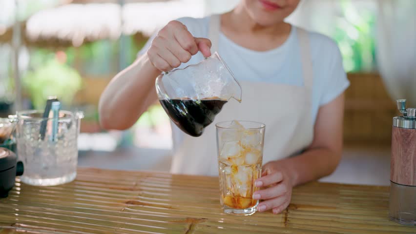 Iced Coffee Preparation, A barista hand pours cold brew coffee over ice in a glass, crafting a refreshing summer beverage.