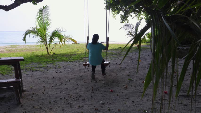 isolated girl enjoying sea side wood swing with bright sky at morning video is taken at Radhanagar Beach at Havelock Island in the Andaman and Nicobar Islands.