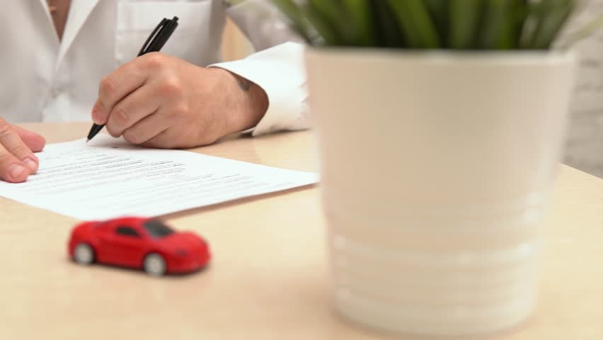 Man buying or selling car. Businessman signing auto insurance document or lease paper. Person writing signature on contract or agreement. Red toy car on the table, selective focus