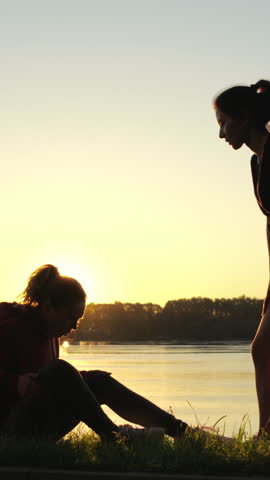 Silhouette of girl giving helping hand to her friend during training. Woman supports and helps another sportsman with trauma or health problems after running. Mutual assistance and teamwork in sport.