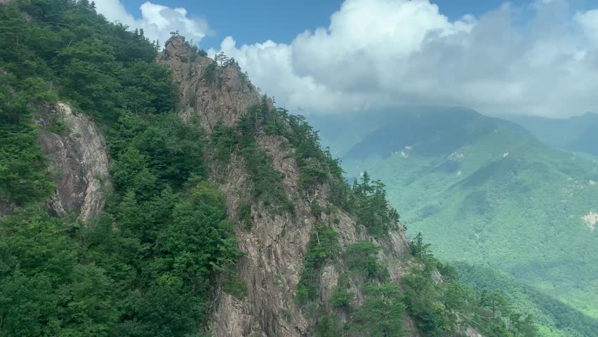 Aerial panoramic, scenic view of Seoraksan National Park mountains covered with green trees and clouds. View from a moving cable car. Summer time. Seoraksan National Park, South Korea