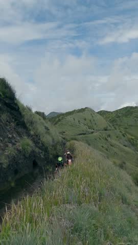 Vertical video. FPV freestyle drone around extreme moto enduro riders group travel race on mountain ridge dirt path hilly valley aerial view. Motorcycle motocross bike people riding dirt road rocky 4k