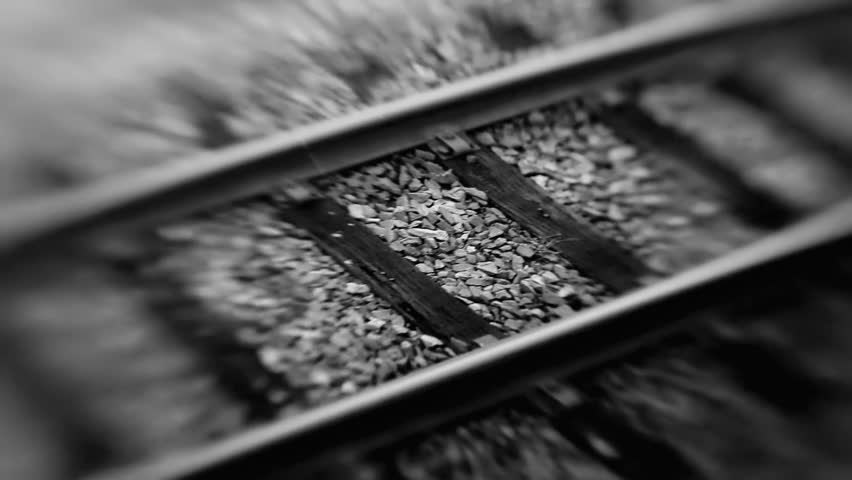 Black and white close-up of railway tracks, showing gravel and metal rails, emphasizing texture and perspective in a classic and timeless view of rail infrastructure