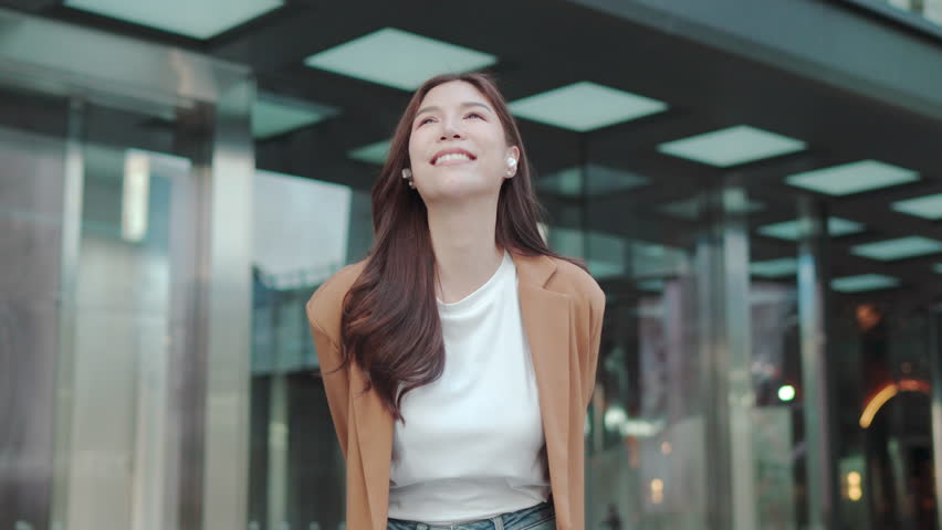 Asian Beautiful woman listening music with earbuds. Dancing outdoors Relaxing, Smiling and Hapiness businesswoman lifestyle. Young Gen Z girl asia people. Relaxation and Cheerful Vibes