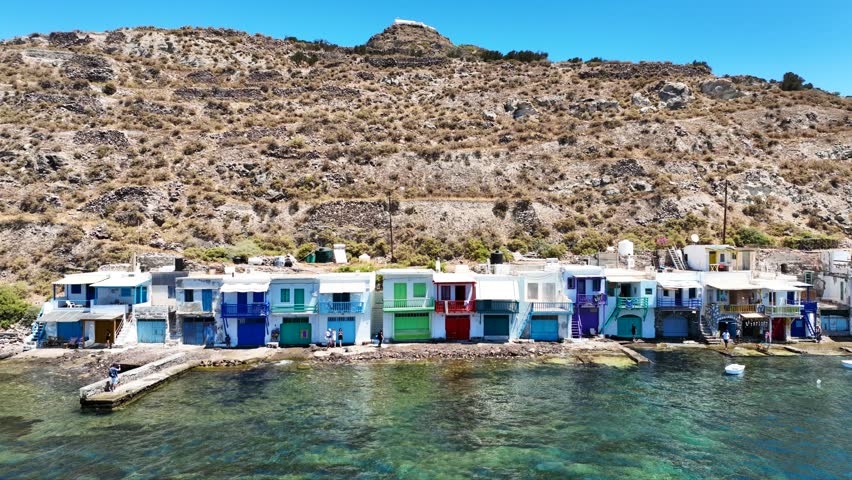 Aerial drone cinematic video of iconic and picturesque fishing village of Klima built by the shore with colourful traditional fishing boat houses called syrmata in island of Milos, Cyclades, Greece
