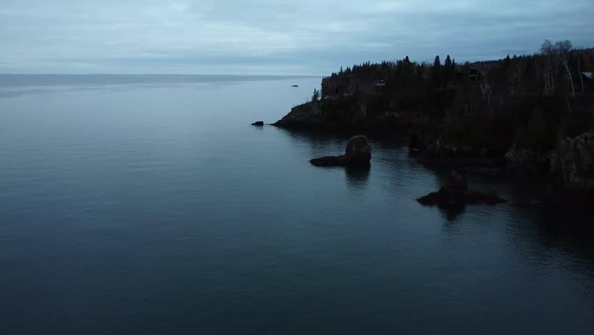 Foggy landscape of forested cliffs on calm lake in Minnesota. The cloudy blue sky reflected in the calm waters of the lake.