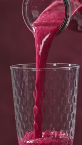 freshly made red banana and berries smoothie flows into a glass from a bottle on a sunny red background