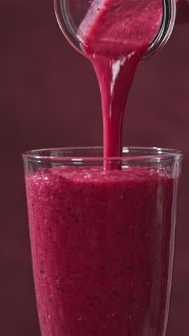 freshly made red banana and berries smoothie flows into a glass from a bottle on a sunny red background