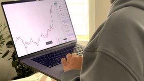 A young man wearing a hoodie analyzes a Bitcoin price chart on his laptop. The chart shows a bullish trend, suggesting a strong market. Natural light and plants enhance the workspace setting. - Powered by Shutterstock - Get 15% off with code: PIKWIZARD15