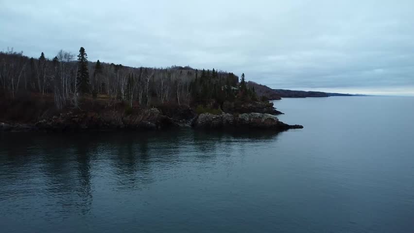 Scenic view of a calm lake in Minnesota, surrounded by rocky shorelines and forested landscapes under an overcast sky