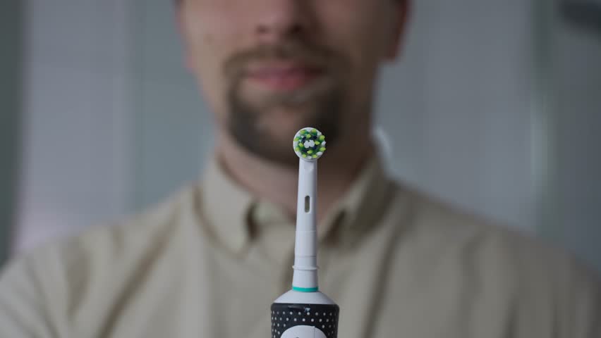 A close-up of a man holding a sleek black electric toothbrush, turning it on and off. Highlighting modern oral hygiene, ultrasonic cleaning technology, and advanced dental care for healthy teeth. 