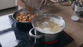 Closeup of unrecognizable person frying vegetables in pan, stirring them with wooden spoon, while spaghetti boiling nearby on modern cooktop in bright, cozy kitchen setting - Powered by Shutterstock - Get 15% off with code: PIKWIZARD15