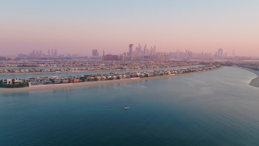 A breathtaking aerial view captures the stunning beauty of Palm Jumeirah, showcasing its luxurious residences and the beautiful serene waters of the UAE, specifically at sunset