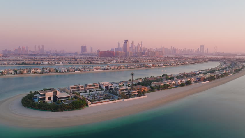 A breathtaking aerial view captures the stunning beauty of Palm Jumeirah, showcasing its luxurious residences and the beautiful serene waters of the UAE, specifically at sunset