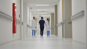 Three healthcare professionals walking down a brightly lit hospital corridor, viewed from behind. Concept of teamwork in medical environments, professional collaboration, modern healthcare facilities - Powered by Shutterstock - Get 15% off with code: PIKWIZARD15