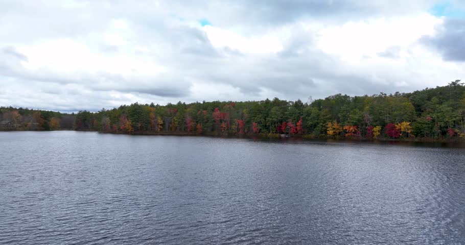 Aerial view over water toward fall trees on the shoreline of Lake Winnipesaukee