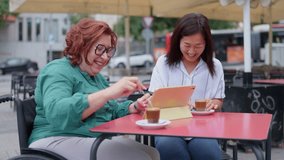 Engaging moment of a woman using a tablet alongside her friend at a lively outdoor cafe - Powered by Shutterstock - Get 15% off with code: PIKWIZARD15