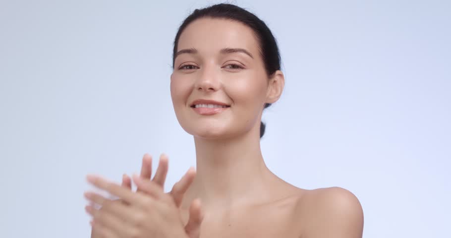A beautiful young woman smiling with hands on her face, showcasing flawless skin. Perfect for skincare ads, natural beauty promotions, or wellness branding. Professional studio video.