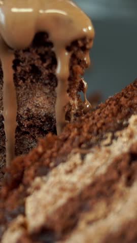 Close up of chocolate cream flows on freshly baked chocolate cake with nut and lemon filling. Food dessert background. Vertical shot