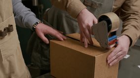 Tilt up shot of two male coffee roastery workers packing boxes with tape while preparing for shipping at factory - Powered by Shutterstock - Get 15% off with code: PIKWIZARD15
