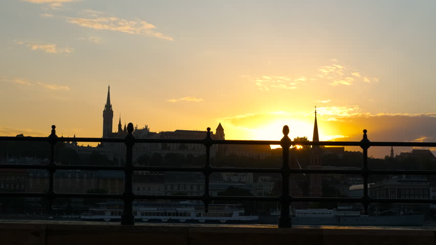 Tram passing by at sunset. The silhouette of a tram passing by on a bridge over the danube river. Buda castle and matthias church are in the distance