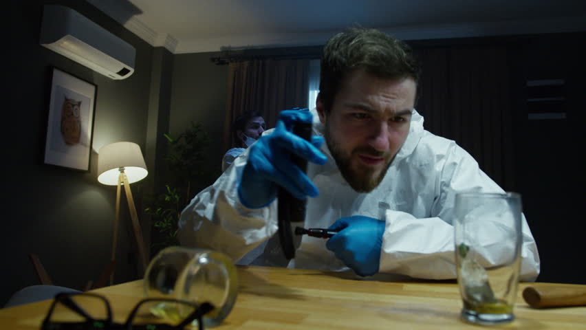 A forensic investigator examines a piece of evidence closely with a flashlight at a crime scene. Another investigator is in the background, creating a focused crime scene analysis atmosphere.