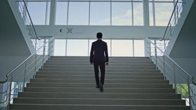 Elegant entrepreneur climbing stairs in bright modern office back view. Professional male executive moving upward with focused ambition in light interior. Corporate leader ascending stairway in suit. - Powered by Shutterstock - Get 15% off with code: PIKWIZARD15