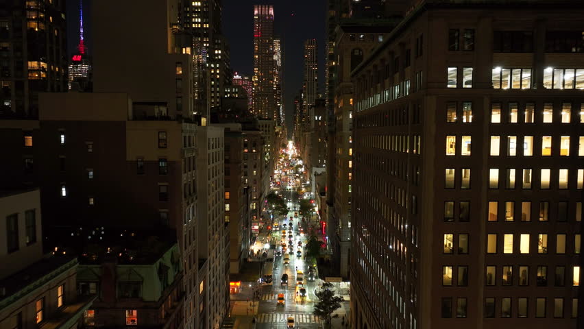 Aerial views capture Park Avenue in the Upper East Side of New York City at night. Cars move along street adorned with luxury apartment buildings