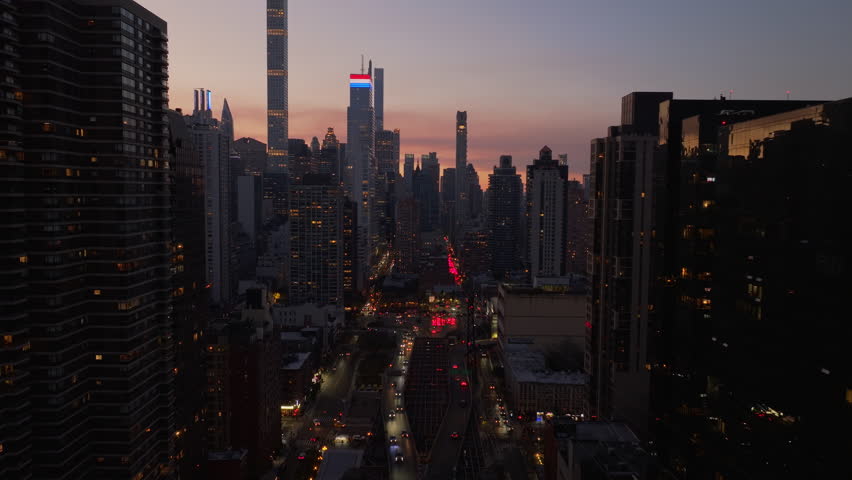 Aerial view of Manhattan, New York City skyline and Queensboro Bridge at sunset. Modern skyscrapers stand tall in the distance as traffic moves along the streets below