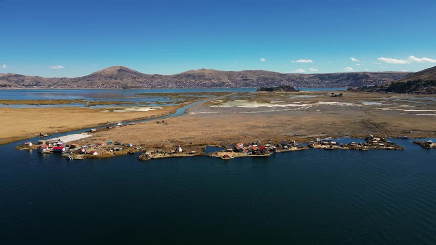 Drone footage of Lake Titicaca, Peru, showcasing floating villages, traditional boats, huts, islands, and the breathtaking Andes mountains in the background. Perfect for scenic and cultural visuals.