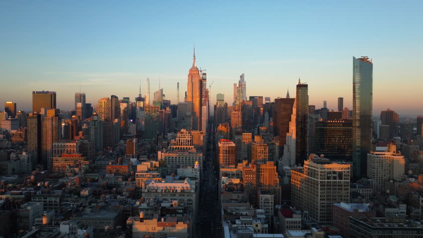 Warm sunlight envelops New York City's skyscrapers of Midtown Manhattan, including Empire State Building. Sun sets on the horizon on a breathtaking urban scene at dusk