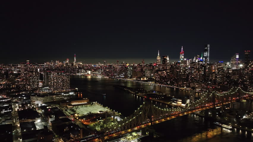 Camera pans over the illuminated Queensboro Bridge and East River at night, showcasing New York City skyline with traffic from Queens to Manhattan