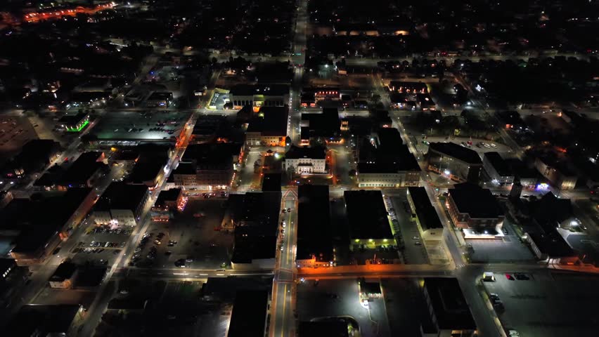 Small american town with straight avenues at night. American housing area with warm lighting streetlamps. Aerial top down panning.