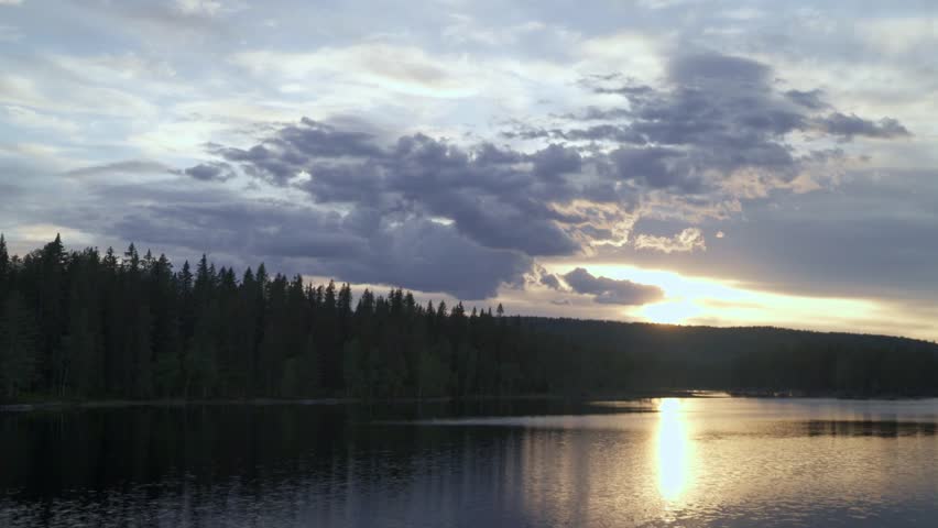 Sunset over a tranquil forest lake with golden reflections and dramatic clouds in the sky.